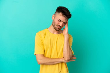 Kafkasyalı genç adam mavi arka planda izole edilmiş, baş ağrısı var.