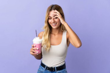 Mor arka planda izole edilmiş çilekli milkshake 'li genç sarışın Uruguaylı kadın gülüyor.