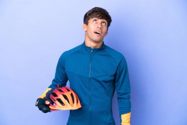 Mor arka planda izole edilmiş genç beyaz adam yukarı bakıyor ve şaşırmış bir ifadeyle