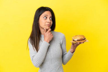 Sarı arka planda, elinde hamburger tutan beyaz bir kadın şüpheleri var.