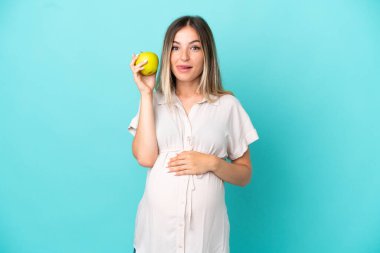 Genç Romen kadın mavi arka planda izole edilmiş hamile ve elinde bir elma tutuyor