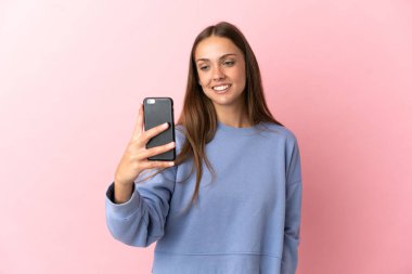 Soyutlanmış pembe arka planı olan genç bir kadın selfie çekiyor.