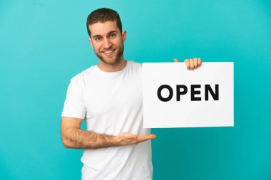 Yakışıklı sarışın, izole edilmiş mavi arka plan. Elinde mutlu bir ifadeyle açık yazılı bir pankart var.