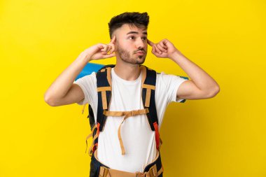 Sarı arka planda izole edilmiş büyük sırt çantalı genç bir beyaz adam kuşkuları ve düşünceleri var.