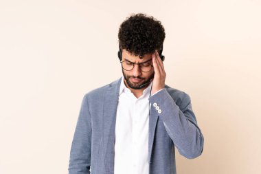 Faslı bir pazarlamacı bej arka planda başağrısı olan bir kulaklıkla çalışıyor.