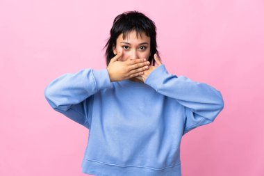 Genç Uruguaylı kadın izole edilmiş pembe arka planda ağzı elleriyle kapatıyor.