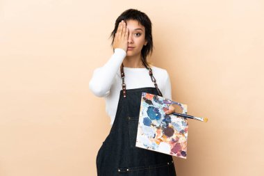 Genç bir ressam, arka planda bir palet tutuyor ve bir gözü elle kapatıyor.