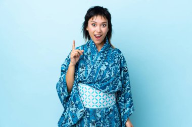 İzole edilmiş mavi arka planda kimono giyen genç bir kadın parmağını kaldırarak çözümü anlamaya çalışıyor.