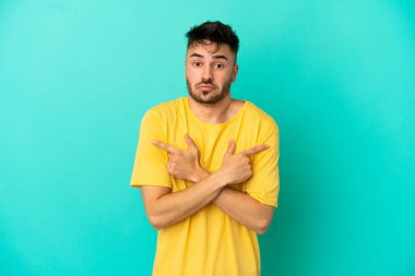 Mavi arka planda izole edilmiş genç beyaz adam, yan taraftakilerin şüphelerine işaret ediyor.