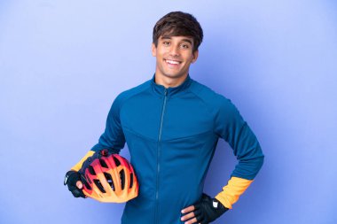 Mor arka planda izole edilmiş, kolları kalçasında poz veren ve gülümseyen genç beyaz bir adam.