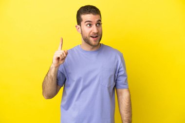 Sarışın, izole edilmiş sarı arka plandaki yakışıklı adam parmağını kaldırarak çözümü bulmaya çalışıyor.