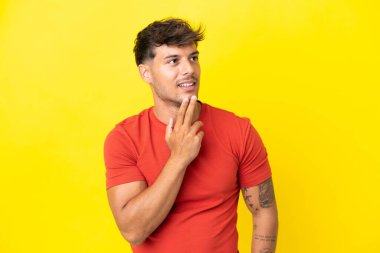 Beyaz tenli yakışıklı adam sarı arka planda izole edilmiş gülümserken yukarı bakıyor.