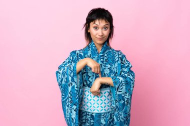 İzole edilmiş mavi arka planda kimono giyen genç bir kadın geç kalma jesti yapıyor.