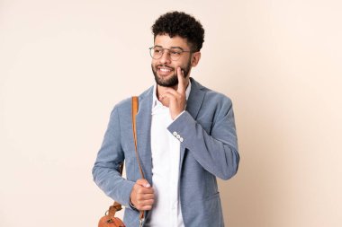 Faslı genç bir iş adamı bej arka planda izole edilmiş, araştırırken bir fikir düşünüyor.