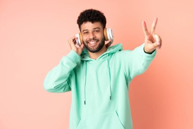 Genç Faslı bir adam pembe arka planda izole edilmiş müzik dinliyor ve şarkı söylüyor.