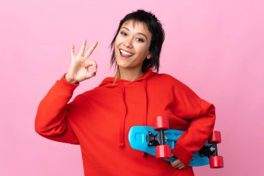 Genç Uruguaylı kadın pembe arka planda paten kayıyor ve iyi işareti yapıyor.