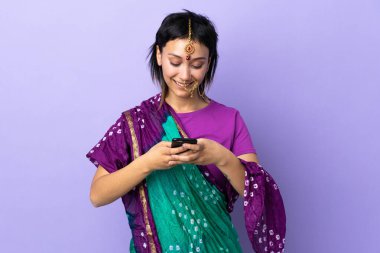 Mor arka planda izole edilmiş Hintli bir kadın cep telefonuyla mesaj gönderiyor.