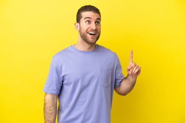 Sarışın yakışıklı adam izole edilmiş sarı arka planda yukarı bakıyor ve şaşırıyor.