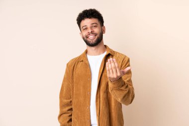 Faslı genç bir adam, bej arka planda izole edilmiş, bizimle gelmesi için davet ediliyor. Gelmene sevindim.