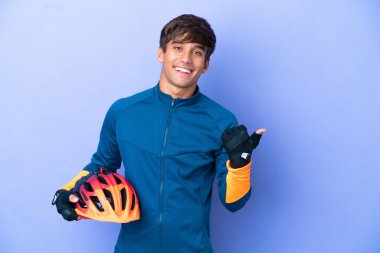 Mor arka planda izole edilmiş genç bir beyaz adam bir ürünü sunmak için yan tarafı işaret ediyor.