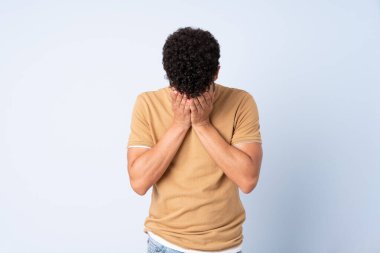 Faslı genç bir adam mavi arka planda izole edilmiş, yorgun ve hasta bir ifadeyle.