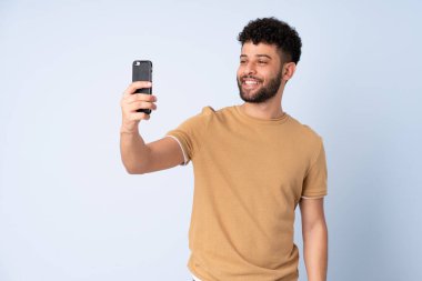 Mavi arka planda izole edilmiş genç Faslı bir adam selfie çekiyor.