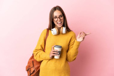 Soyutlanmış pembe arka planda genç bir bayan parmak göstererek bir ürün sunuyor.