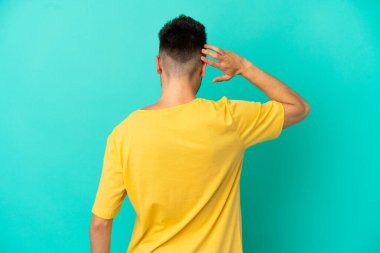 Kafkasyalı genç adam mavi arka planda izole edilmiş ve düşünüyor.