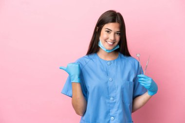 Dişçi kadının elinde pembe arka planda izole edilmiş aletler var. Ürünü sunmak için kenarı işaret ediyor.