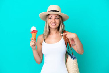 Elinde dondurma ve plaj çantası olan genç Romen kadın mavi arka planda şaşırmış bir yüz ifadesiyle izole edildi