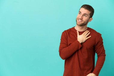 Yakışıklı sarışın, soyutlanmış mavi arka planda gülümserken yukarı bakıyor.