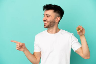 Elinde mavi arka planda izole edilmiş bir Bitcoin tutan genç adam parmağını yana doğru uzattı ve bir ürün sundu.