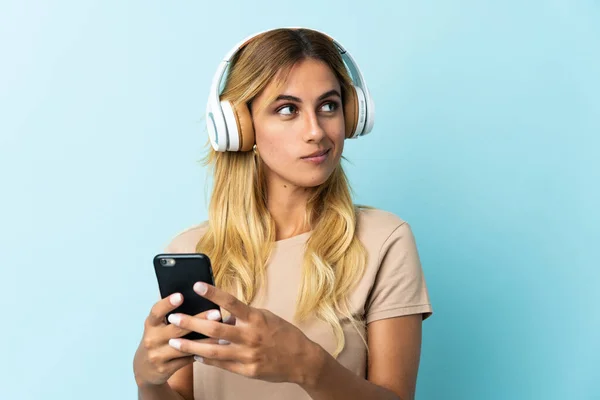 Joven Rubia Uruguaya Aislada Sobre Fondo Azul Escuchando Música Con — Foto de Stock