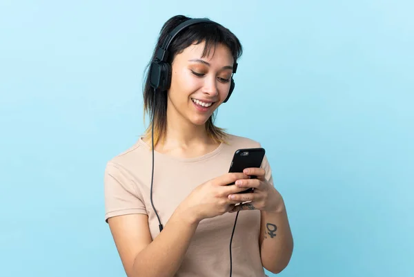 Joven Uruguaya Sobre Fondo Azul Aislado Escuchando Música Mirando Móvil —  Fotos de Stock