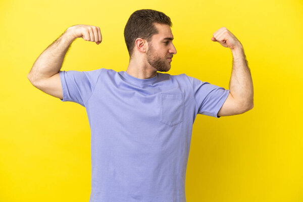 Handsome blonde man over isolated yellow background doing strong gesture