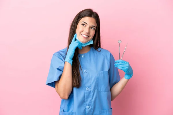 ピンクの背景に隔離されたツールを保持している歯医者の女性は アイデアを考えながら検索 — ストック写真