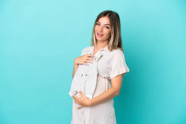 Giovane Donna Rumena Isolata Sfondo Blu Incinta Con Mano Vestiti — Foto Stock