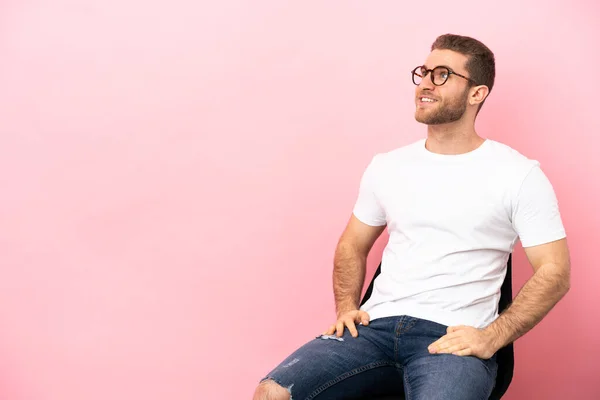 Joven Sentado Una Silla Sobre Fondo Rosa Aislado Pensando Una — Foto de Stock