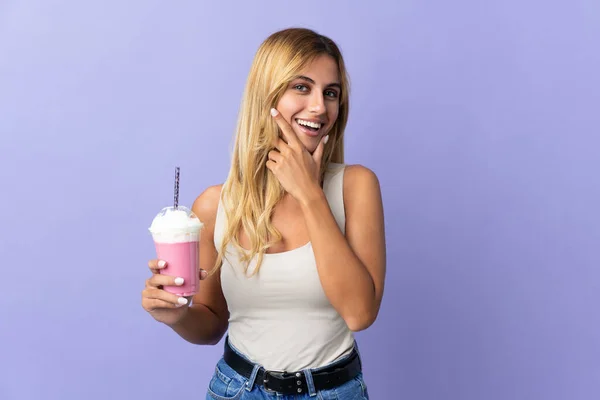 年轻的金发乌拉圭女人 与草莓奶昔隔离在紫色的背景上 快乐而微笑 — 图库照片
