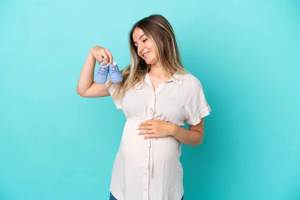 Jovem Romena Isolada Fundo Azul Grávida Segurando Botas Bebê — Fotografia de Stock