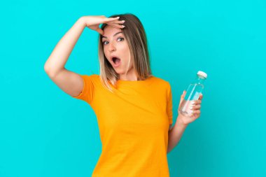 Mavi arka planda izole edilmiş bir şişe suyu olan genç Romen kadın yandan bakarken sürpriz jest yapıyor