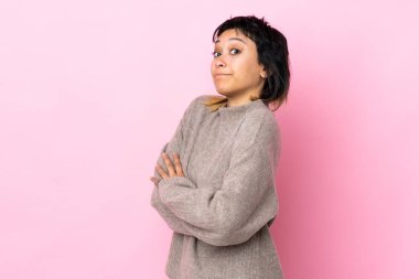 Genç Uruguaylı kadın pembe arka planda, omuzlarını kaldırırken şüpheyle hareket ediyor.
