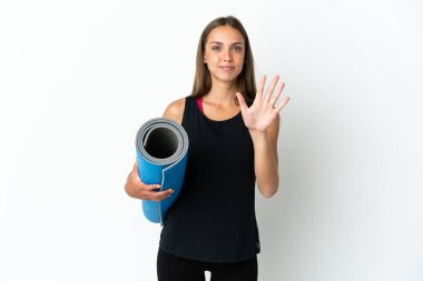 İzole edilmiş beyaz arka plan üzerinde paspas tutarken yoga derslerine giden sporcu kadın parmaklarıyla beşi sayıyor.