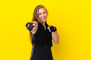 Beyaz arka planda izole edilmiş genç bir İngiliz kadın ön tarafı işaret ediyor ve gülümsüyor.