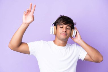 Genç beyaz adam mor arka planda izole edilmiş müzik ve dans dinliyor.