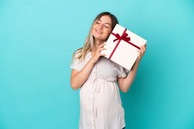 Genç Romen kadın mavi arka planda izole edilmiş hamile ve elinde bir hediye var