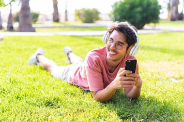 Parkta gezici ve mutlu bir şekilde müzik dinleyen genç beyaz bir adam.