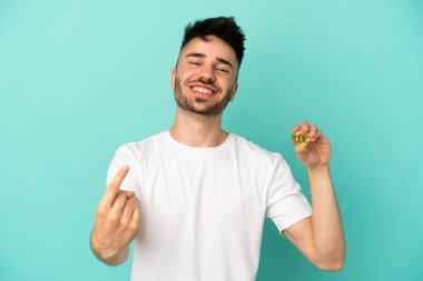 Elinde mavi arka planda izole edilmiş Bitcoin tutan genç adam geliyor.