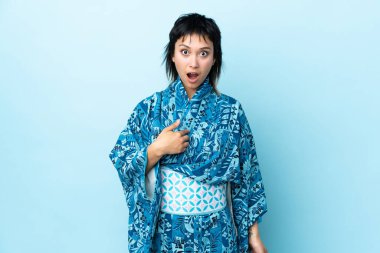 İzole edilmiş mavi arka planda kimono giyen genç bir kadın kendini işaret ediyor.