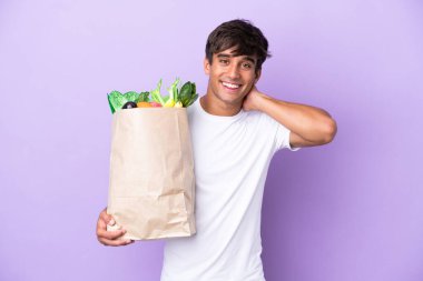 Mor arka planda izole edilmiş alışveriş torbası tutan genç adam gülüyor.